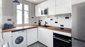 Une cuisine moderne avec des meubles blancs, un réfrigérateur en acier inoxydable, un four à micro-ondes, un four encastré et un lave-linge.