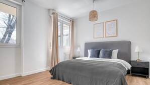 Um quarto moderno com uma cama grande, uma mesa de cabeceira, um abajur e uma janela com cortinas.