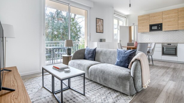 Uma sala de estar moderna com um sofá cinzento, uma mesa de centro e uma área de jantar com uma mesa e cadeiras.