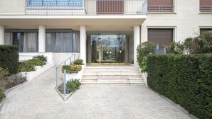 Um edifício moderno com entrada central, uma escadaria que leva à entrada e uma pequena varanda no andar superior.
