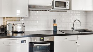 A modern kitchen with white cabinets, a stainless steel range hood, a microwave, a toaster, and a dishwasher. - Blueground | Trocadero, courtyard, nr museums (Paris)