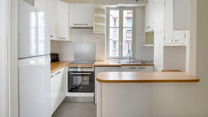 A compact kitchen with white cabinets, a stainless steel oven, a sink, and a window providing natural light. - Blueground | Vaugirard, lively area (Paris)