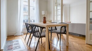 A dining area with a wooden table and chairs, a vase, and a sofa in the background. - Blueground | Vaugirard, lively area (Paris)