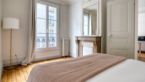 A bedroom with a large bed, a radiator, a fireplace, and a window with curtains. - Blueground | Vaugirard, lively area (Paris)