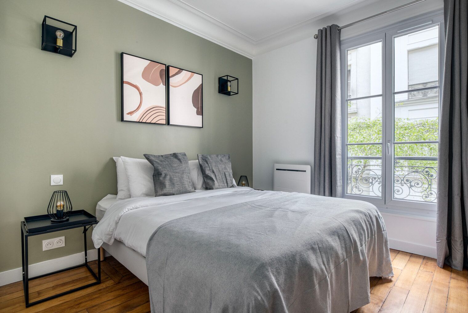 A bedroom with a bed, a bedside table, a lamp, a radiator, and a window with curtains.