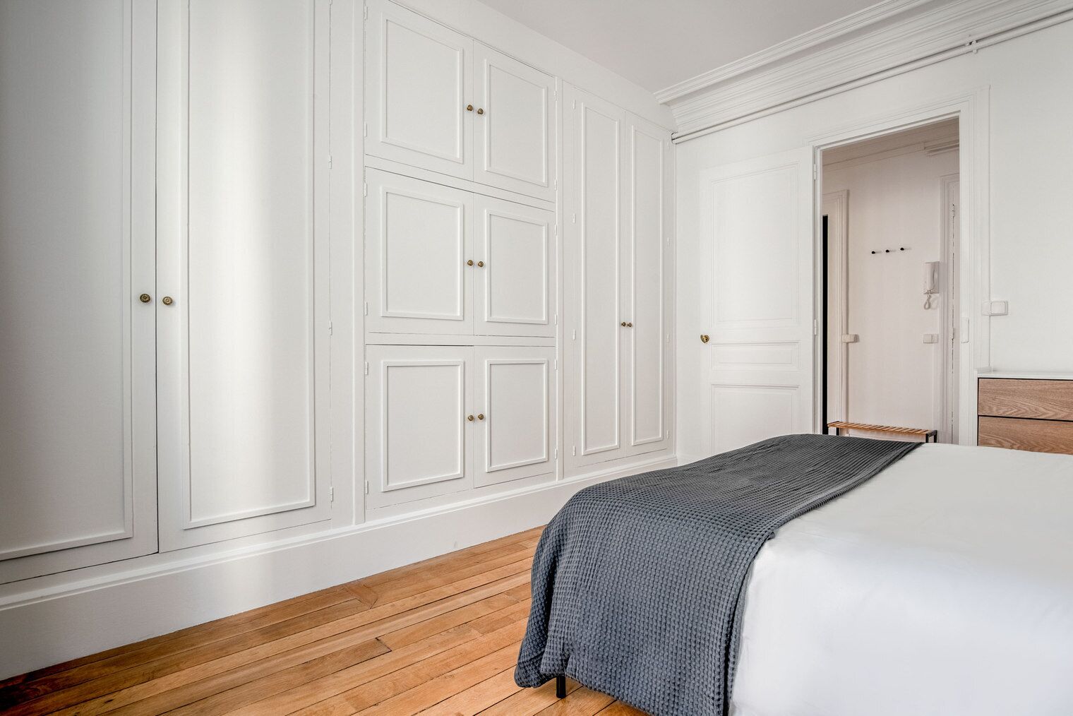Een slaapkamer met een bed, houten vloeren, witte muren en een grote garderobe met meerdere deuren.