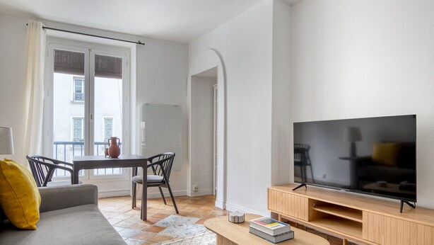 A modern living room with a sofa, TV, coffee table, and a dining area with a table and chairs. - Blueground | Canal St Martin, near cafes & shops (Paris)