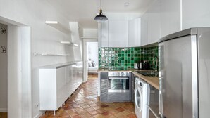 A modern kitchen with white cabinets, a stainless steel refrigerator, a washing machine, and a tiled backsplash. - Blueground | Canal St Martin, near cafes & shops (Paris)