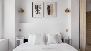 Une chambre moderne avec un grand lit, du linge de lit blanc, deux tables de chevet et deux lampes fixées au mur.