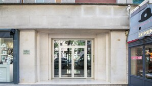 Une façade d’immeuble avec une entrée en verre, une devanture de magasin visible sur la droite et une enseigne indiquant un restaurant.
