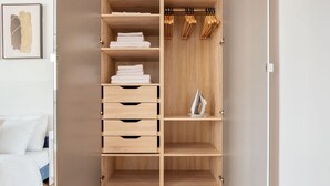 Une armoire en bois avec plusieurs étagères et tiroirs, une tringle pour suspendre les vêtements et une petite planche à repasser.