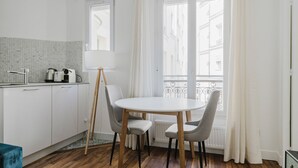 A modern kitchen with white cabinets, a round dining table, and a floor lamp. - Blueground | Commerce, close to offices & shops (Paris)