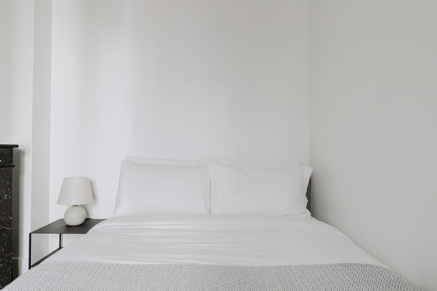 Een minimalistische slaapkamer met een bed, nachtkastje en lamp.