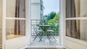 A balcony with a table and chairs, a view of greenery and buildings in the background.