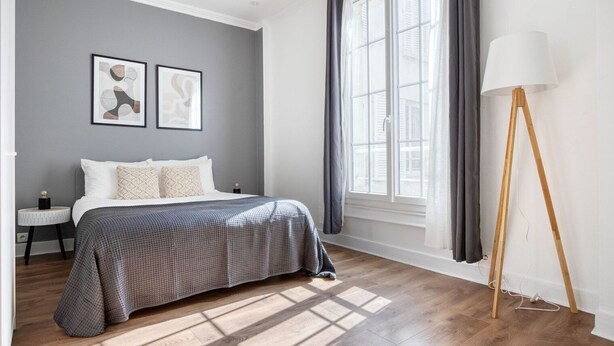 Ein Schlafzimmer mit Bett, Nachttisch, Lampe und einem Fenster mit Vorhängen.