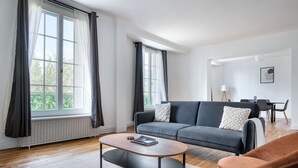 Ein modernes Wohnzimmer mit einem grauen Sofa, einem runden Couchtisch und einem braunen Sessel.