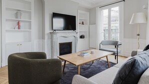 Moderni olohuone, jossa on takka, litteänäyttöinen televisio, sohvapöytä ja sohva.