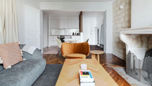 A modern living room with a grey sofa, a wooden coffee table with a book, a small round table, and a fireplace.