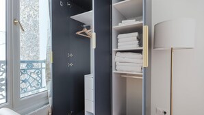A modern room with a large window, a balcony, a wardrobe with hanging space, and a bedside table.