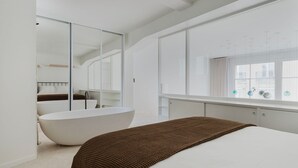 Une chambre moderne avec un grand lit, une baignoire intégrée et un grand miroir.