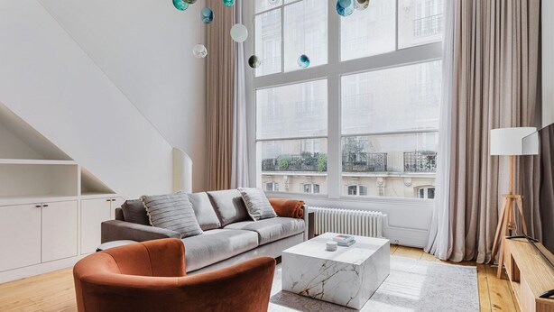 Un salon moderne avec un canapé gris, un fauteuil marron et une table basse en marbre.