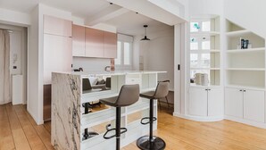 Une cuisine moderne avec des meubles blancs, un plan de travail en marbre et deux tabourets de bar.