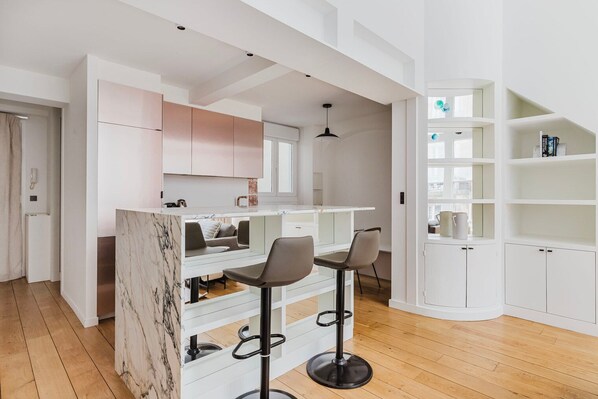 A modern kitchen with white cabinets, a marble countertop, and two bar stools.