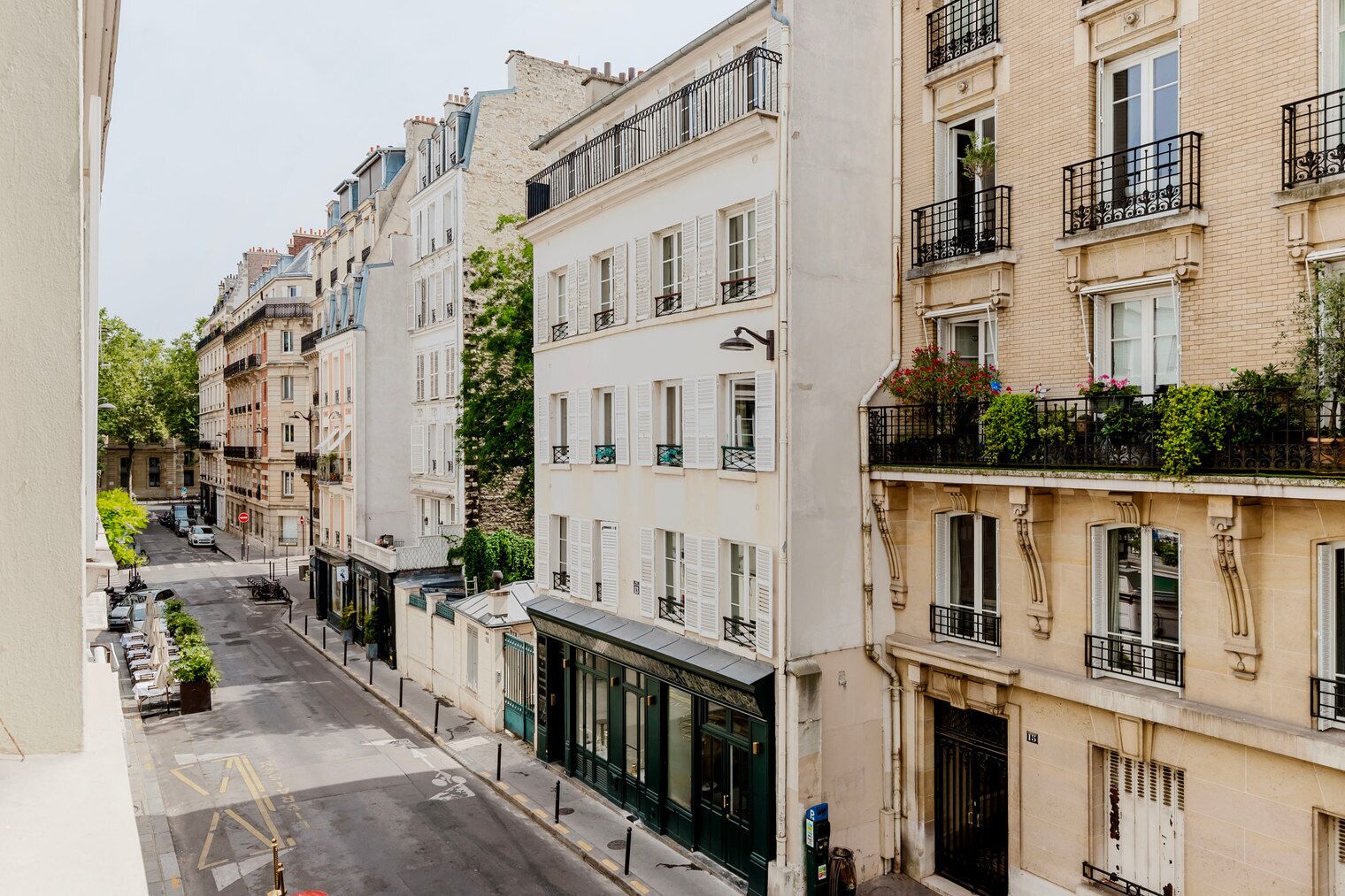 Una hilera de edificios de varios pisos con balcones, una calle en medio y automóviles estacionados.