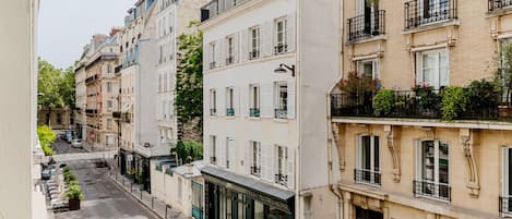 Una hilera de edificios de varios pisos con balcones, una calle en medio y automóviles estacionados.