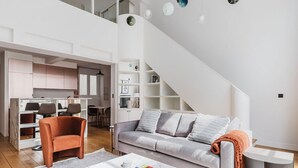 Un salon moderne avec un canapé gris, un fauteuil marron et une table basse blanche. Un escalier mène à un niveau supérieur.