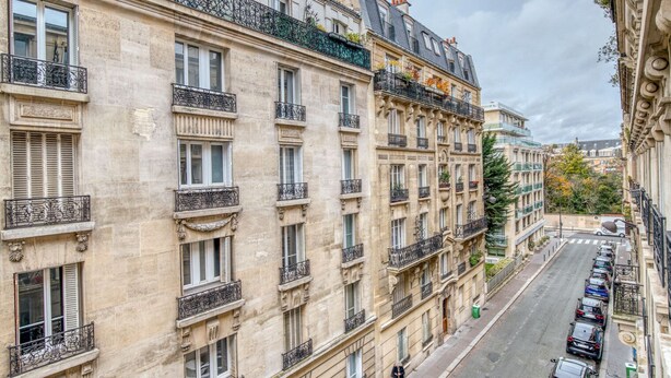Un edificio a più piani con balconi, vista sulla strada e auto parcheggiate.
