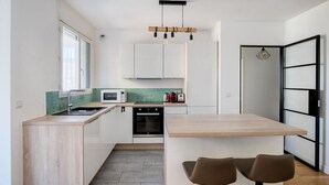 A modern kitchen with a wooden island, white cabinets, a microwave, a toaster, and a hanging light fixture. - Blueground | Gibauderie, balcony, nr station (Paris)