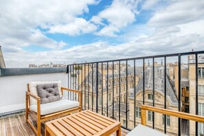A balcony with a wooden chair and table, offering a view of historic buildings and a clear sky. - Blueground | La Marais, balcony, nr shopping (Paris)
