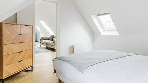 A bedroom with a sloped ceiling, a wooden wardrobe, a bed with a white cover, and a skylight. - Blueground | Les Halles, close to Eiffel Tower (Paris)