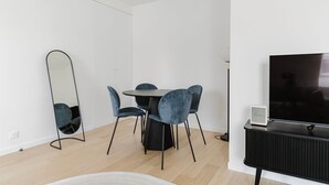 A modern living room with a round dining table, four blue chairs, a large flat-screen TV, a black console, and a floor lamp. - Blueground | Les Halles, close to Eiffel Tower (Paris)