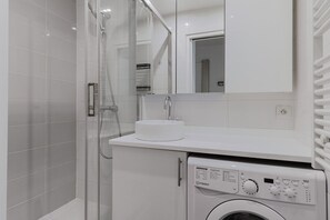 Ein modernes Badezimmer mit einer Duschkabine, einem Waschbecken und einer integrierten Waschmaschine.