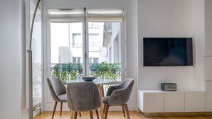 A modern living room with a dining area, a TV on the wall, and a balcony with plants. - Blueground | Porte Dauphine, near shops & food (Paris)