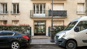 A building with a central entrance, a small balcony, and a parking area with two cars. - Blueground | Porte Dauphine, near shops & food (Paris)