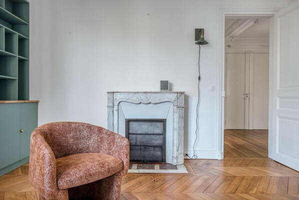 A room with a fireplace, a green shelving unit, and a wooden herringbone floor.