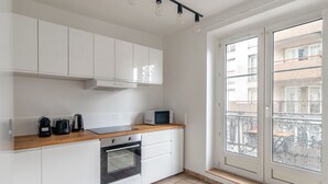 A modern kitchen with white cabinets, a wooden countertop, a microwave, and an oven. - Blueground | Buttes-Chaumont, walk to garden (Paris)