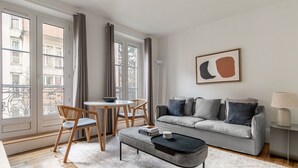 A modern living room with a grey sofa, a round coffee table, and a dining table with chairs. - Blueground | Buttes-Chaumont, walk to garden (Paris)
