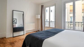 A bedroom with a large bed, a mirror, a radiator, and a window with a balcony view. - Blueground | Buttes-Chaumont, walk to garden (Paris)