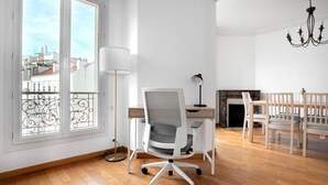A modern living room with a large window, a fireplace, a dining area with wooden chairs, and a white office chair. - Blueground | La Motte-Picquet Grenelle, near shops (Paris)