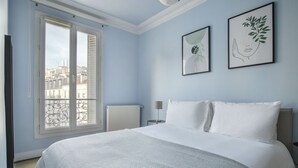 A bedroom with a large bed, a radiator, a window with a view of buildings, and two framed artworks on the wall. - Blueground | La Motte-Picquet Grenelle, near shops (Paris)