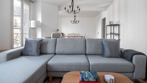 A modern living room with a grey sectional sofa, a wooden coffee table with books, a chandelier, and a dining area in the background. - Blueground | La Motte-Picquet Grenelle, near shops (Paris)