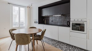 A modern kitchen with white cabinets, a black backsplash, and a round dining table with chairs. - Ternes, nr the Champs Elysées (Paris)