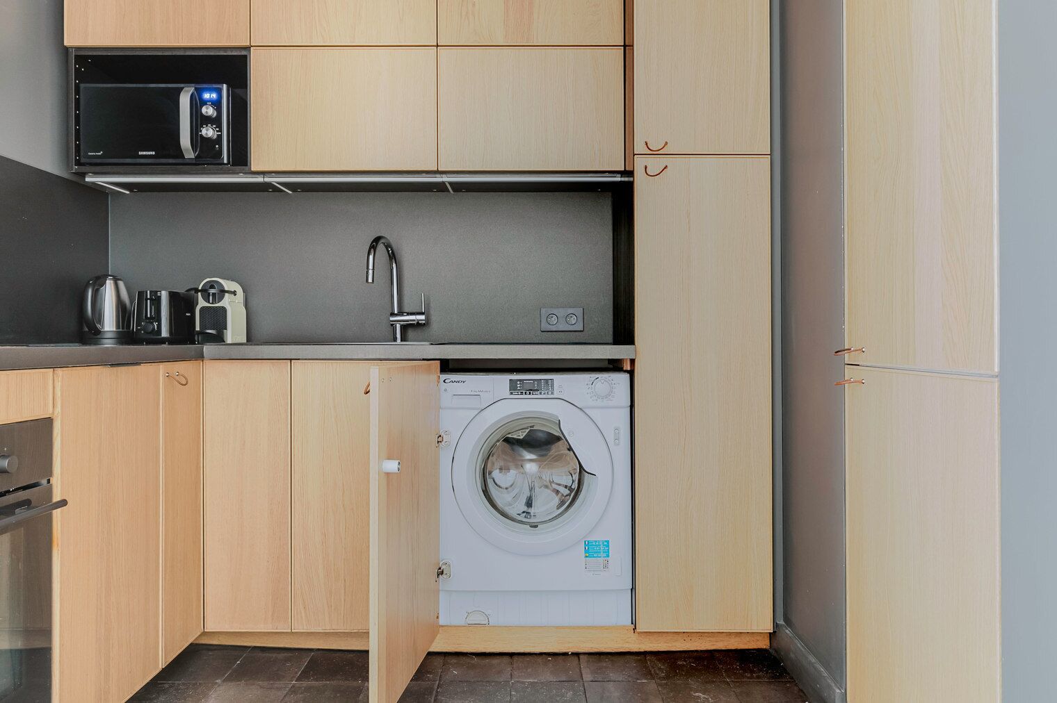 A compact kitchen with a microwave, kettle, and washing machine.