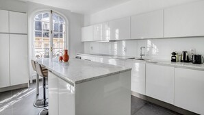 Une cuisine moderne avec des meubles blancs, un îlot en marbre et une grande fenêtre qui laisse entrer la lumière naturelle.