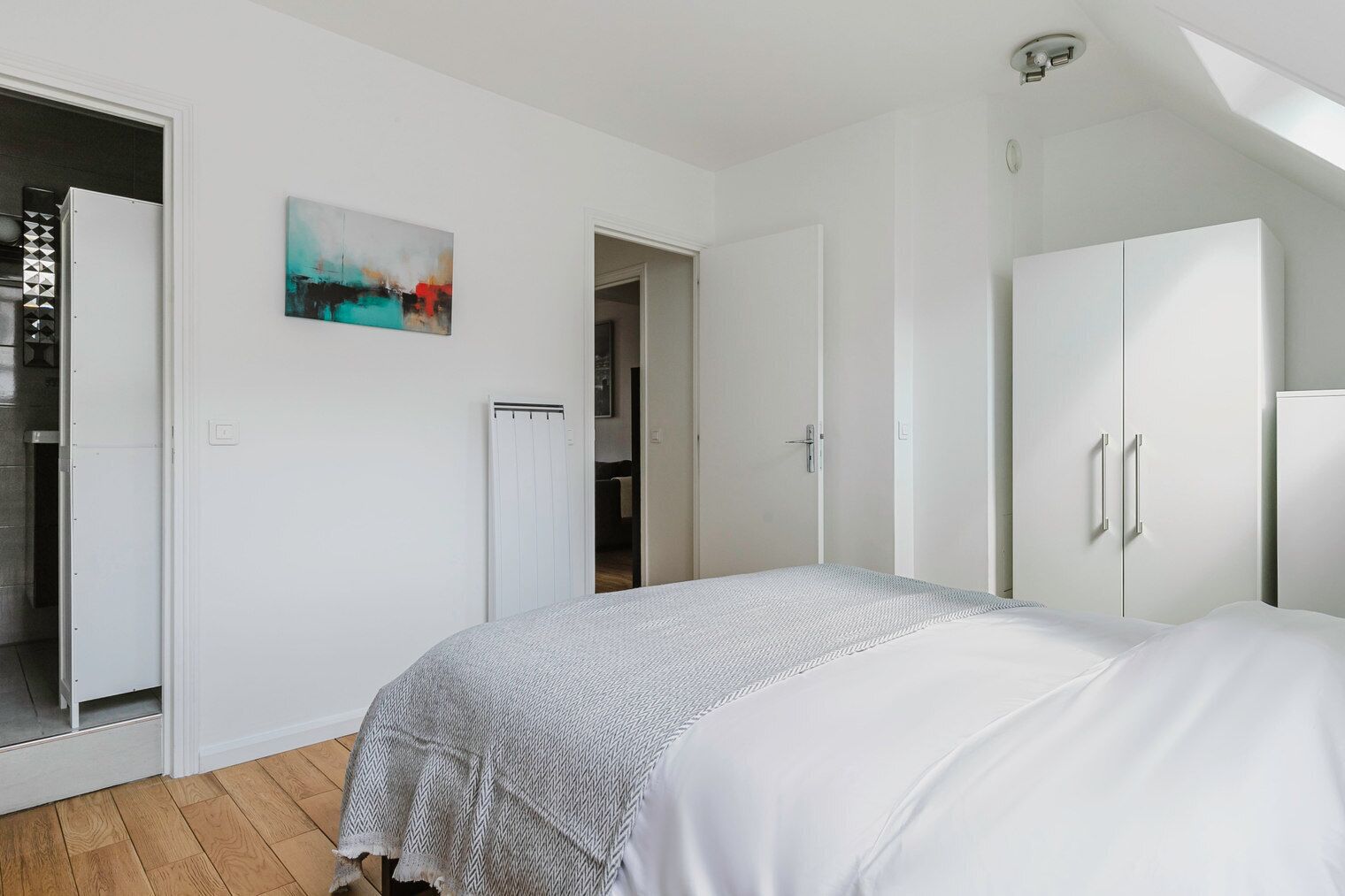 Une chambre à coucher comprenant un lit, une armoire, un radiateur et une porte donnant sur une autre pièce.