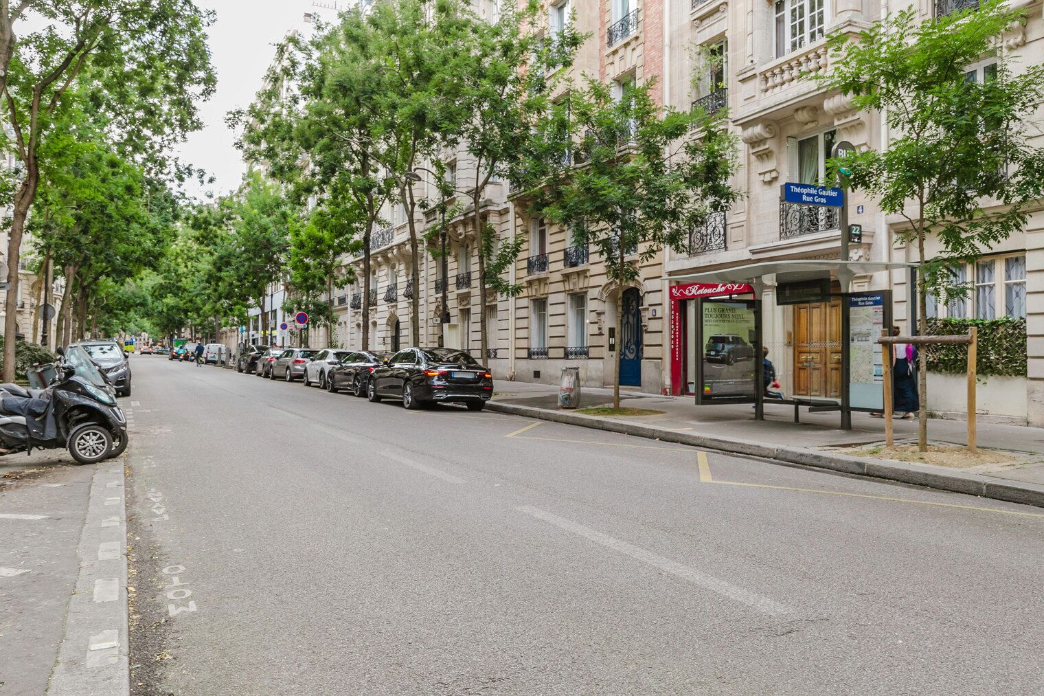 A street lined with parked cars and trees, with a building featuring a sign for 'Theophile Gautier Rue Gros'.